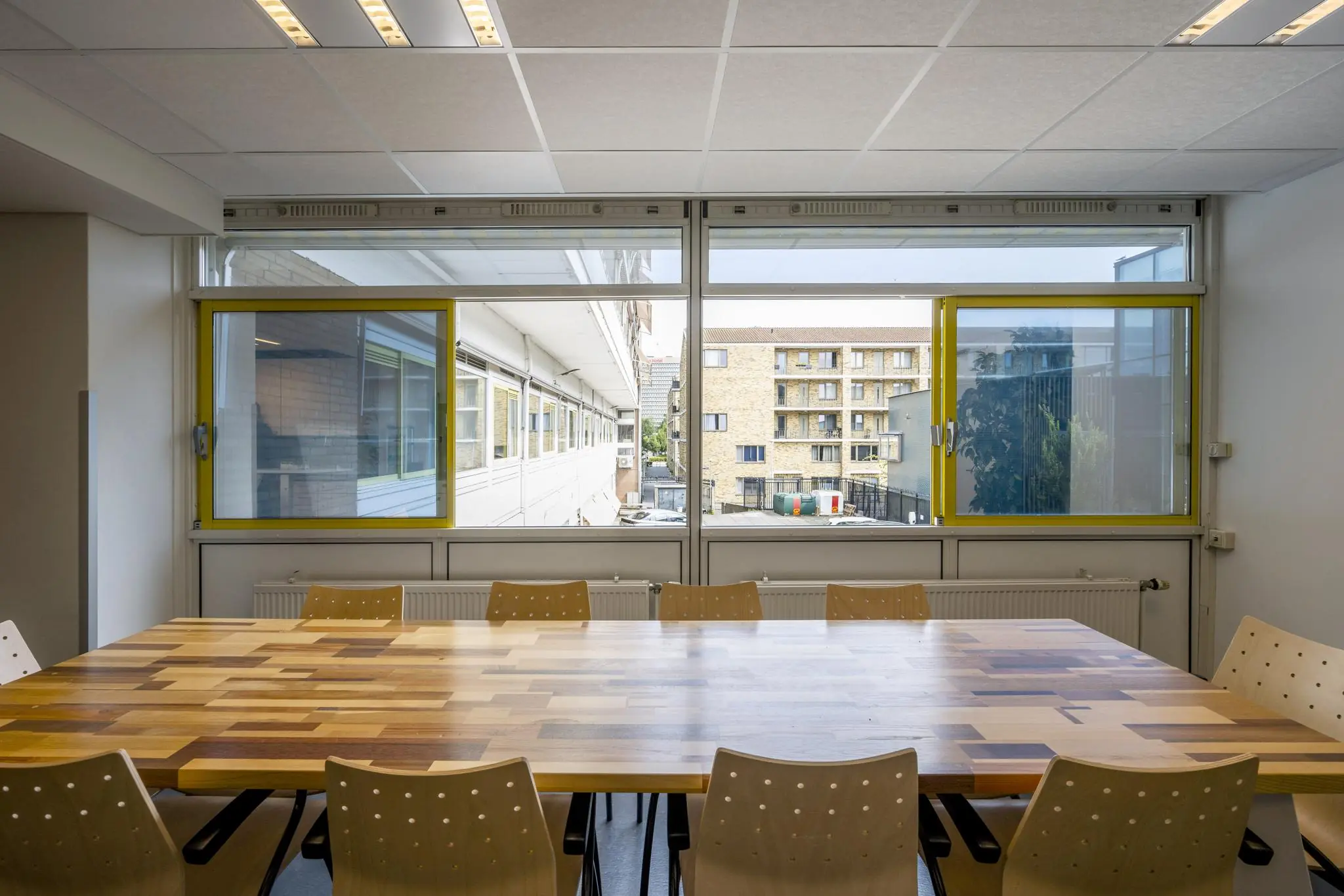 Vergaderruimte met houten tafel en stoelen aan de Jan Tooropstraat, met uitzicht op aangrenzende gebouwen.